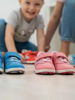 Variedad de calzado infantil de diferentes colores y tallas, con un niño probándose un zapato.