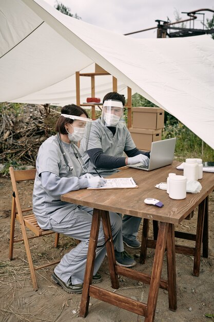 A group of aid workers using satellite phones and laptops in a field tent, coordinating relief efforts after a tornado in Oklahoma.