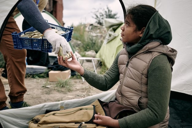 A USAID relief worker distributing water bottles to displaced refugees in a camp. The scene shows a dusty, arid environment with tents in the background, illustrating USAID's work in international disaster zones.