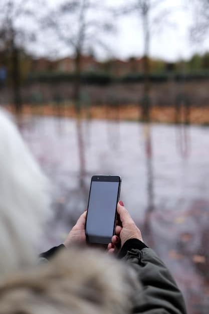 A hand holding a smartphone displaying a weather alert, with the background showing a blurry image of a neighborhood.