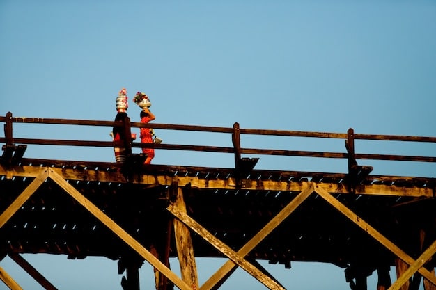 Construction workers rebuilding a damaged bridge in Puerto Rico after a hurricane. Heavy machinery is being used to replace sections of the bridge, and engineers are overseeing the operation. The surrounding landscape shows signs of damage, with fallen trees and debris.