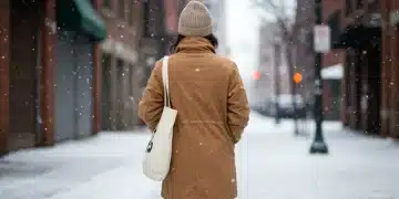 Mujer vistiendo un abrigo sostenible en un paisaje invernal urbano de Estados Unidos.